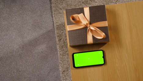 Overhead-Shot-Man-Picking-Up-Gift-Wrapped-Present-From-Table-At-Home-With-Green-Screen-Mobile-Phone